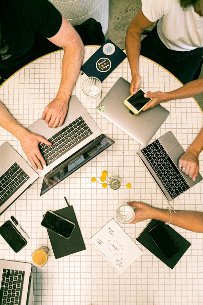 Top view of a team collaborating with laptops, phones, and notes in a modern workspace.